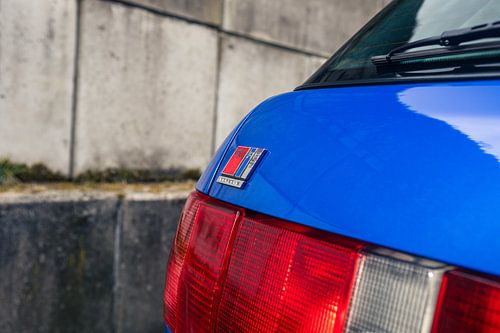 Audi RS2 bleue sur une longue route près d'un mur historique