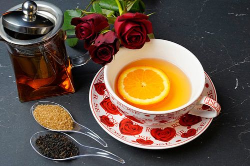 Zwarte thee geserveerd met sinaasappelschijfje en rode rozen