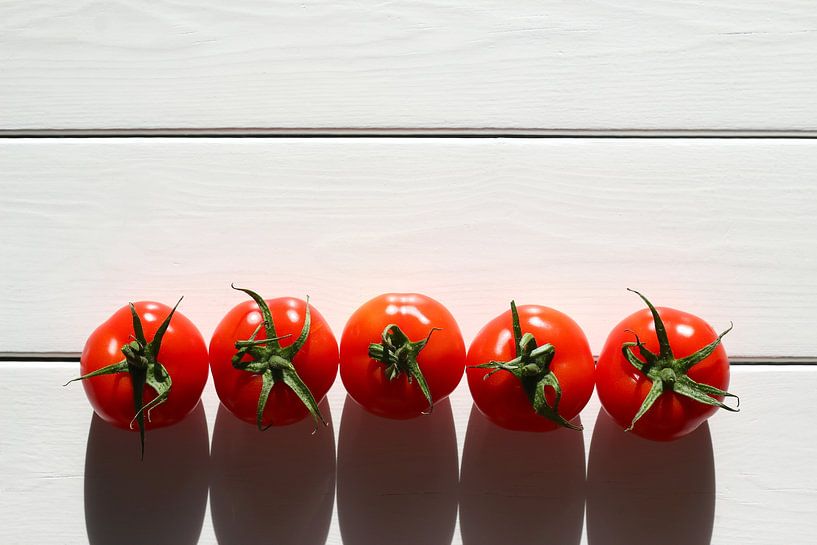 Vijf tomaten op een rij in de zon op een houten tafel van Maarten Pietersma