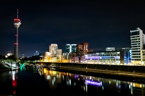 Düsseldorf’s Medienhafen at night, featuring Gehry’s buildings, the Rhine Tower and the illuminated harbour basin / marina