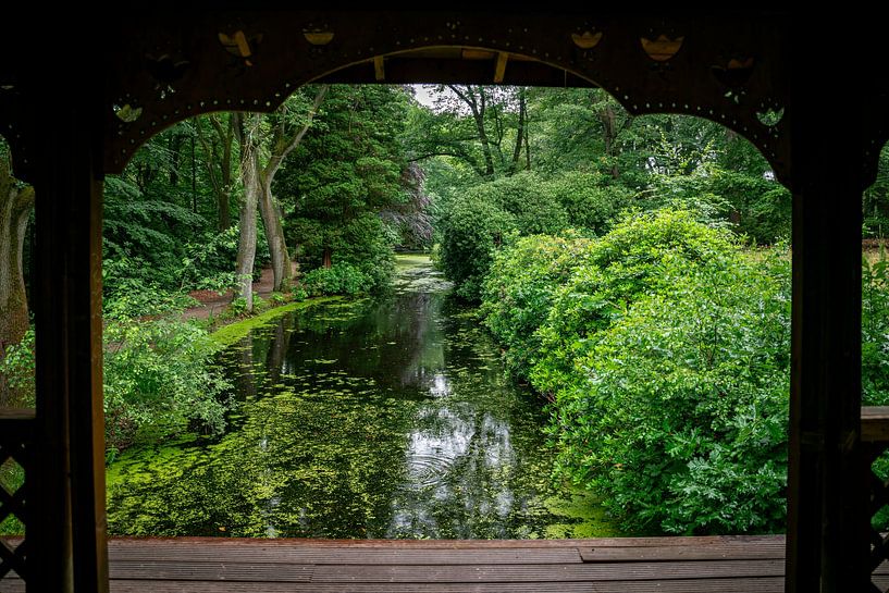 a view through a wooden pergola on a pond bordered by trees with red and green foliage by ChrisWillemsen