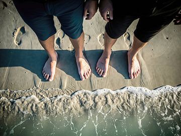 Two Pairs of Feet on Beach Sand at Water's Edge by Markus Gann