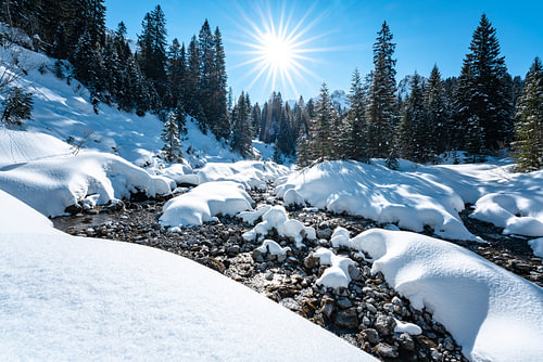 Sunny view with beautiful snow and river in Kleinwalsertal valley