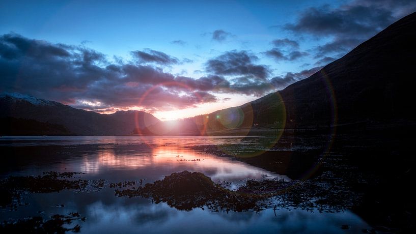 der letzte Sonnenstrahl des Tages über dem windstillen See in Schottland von Hans de Waay