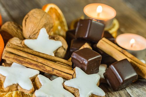 De vormkoekjes van de Kerstmisster, chocolade, noten, kaneel en kaarsen op houten lijst