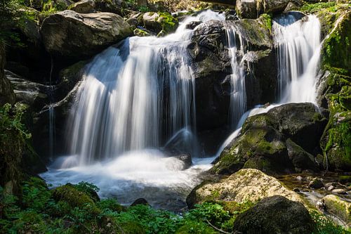 Soleil brillant sur des chutes d'eau entre des rochers verts panorama