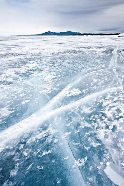 Crossed cracks of transparent ice on Lake Baikal, distant mountains, harsh sky by Michael Semenov