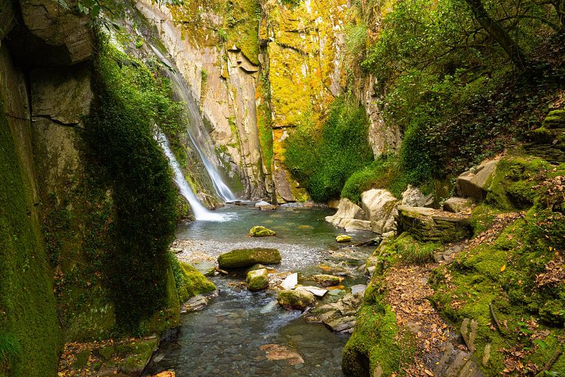 A majestic waterfall cascading down between overgrown rocks. by Wolbert Erich