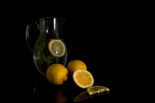 still life with a jug of water filled with mint and lemon with the raw lemon fruit in the foreground