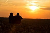 Ein Paar sitzt auf der Wiese und schaut in den Sonnenuntergang von Frank Herrmann Miniaturansicht
