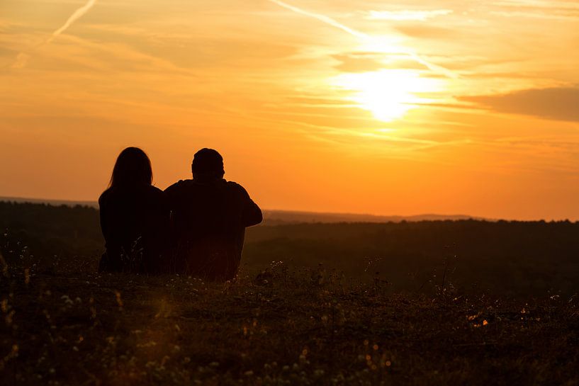 Ein Paar sitzt auf der Wiese und schaut in den Sonnenuntergang von Frank Herrmann