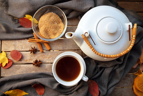 Teetasse und eine weiße Teekanne auf einem Holztisch mit Gewürzen und einigen Herbstblättern, Hochwi