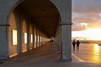 De lage winterzon komt onder de wolken vandaan en werpt een gouden licht over de boulevard en door de poorten van de arcade.