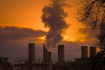 Rokende schoorstenen van een fabriek in de ondergaande zon van ManfredFotos