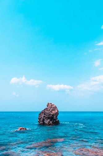 Een eenzame rots steekt uit het azuurblauwe water.