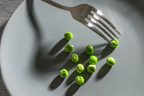 Einige grüne Erbsen und eine Gabel mit Schatten auf einem grauen Teller, magere Diätmahlzeit nach de