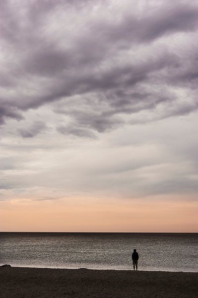 Ein Mensch steht am Strand und genießt nachdenklich die Abendstimmung am Meer von Michael Moser