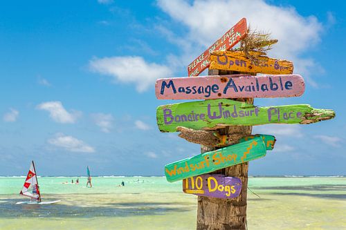 Colorful signpost at coast of Bonaire with windsurfers on sea