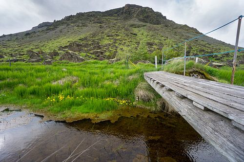 IJsland - Groene berg en enorme stenen met rivier en houten b