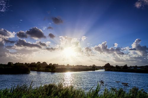 Zonnestralen vanachter de wolken over het water