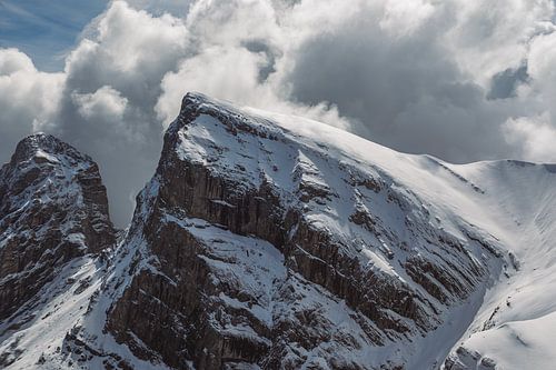 Besneeuwde bergtop tussen de wolken door