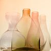 Still life of various glass bottles in warm orange, pink and green hues by Birgitte Bergman