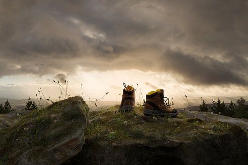 Wandelschoenen liggen op een met vegetatie begroeide rotsrichel tegen een adembenemende achtergrond van wolken in het zonlicht