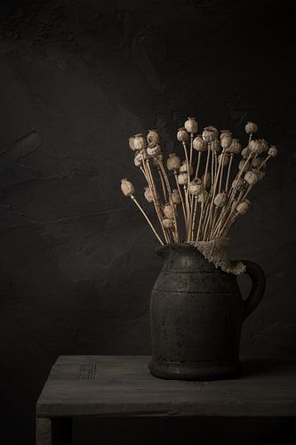 Still life with branches of dried poppy bulbs in grey stone jar (vertical)