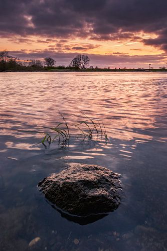 A stone alone in the water during sunset