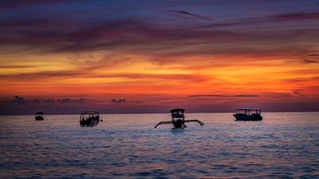 Boats bobbing in the ocean with a fiery sky as background by Rene Siebring