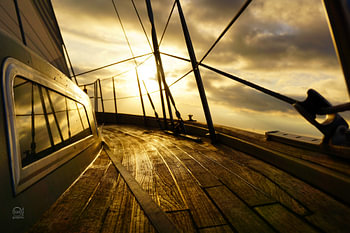 Segelyacht bei Morgensonne und bewölktem Himmel.