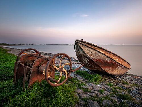 Verweerde boot en roestige lier aan de kust