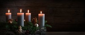 Vier brennende Kerzen auf einem Adventskranz aus Tannenzweigen mit Weihnachtsdekoration vor einer du von Maren Winter