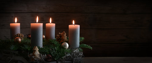 Vier brennende Kerzen auf einem Adventskranz aus Tannenzweigen mit Weihnachtsdekoration vor einer du