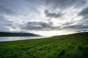 IJsland - Magische wolkenformaties boven het meer achter groen oplichtende velden van adventure-photos