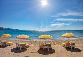 Liegestühle mit gelben Sonnenschirmen am Strand, die Sonne glitzert auf dem Meer, Le Lavandou, Var,
