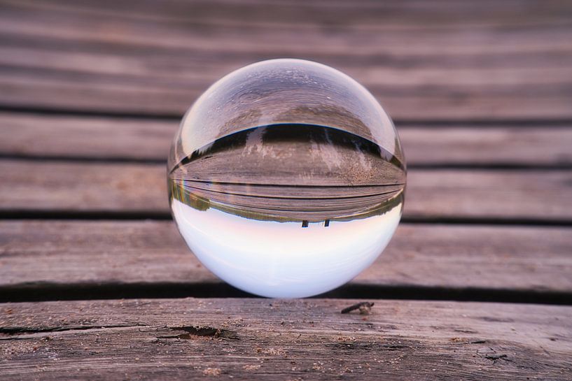 Glass ball on a footbridge reaching into a lake by Martin Köbsch