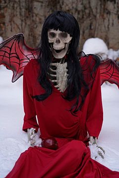 Duivel bruid skelet met rode jurk en duivel vleugels in de sneeuw