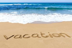 Wort Urlaub geschrieben in Sand auf sandigen Küste mit blauen Meer und Wellen