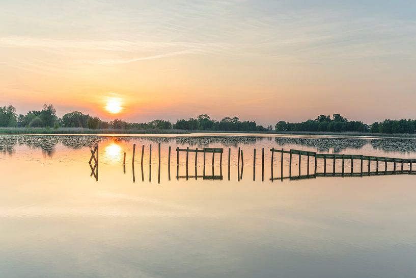 Wooden poles in the water at sunset by Marcel Kerdijk