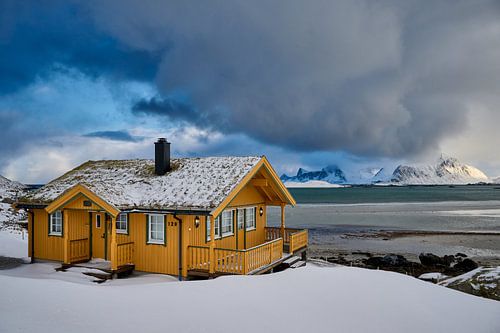 wooden yellow house or hut in winter landscape in stormy weather with sea and mountains
