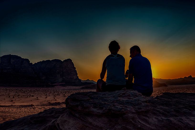 romantisch stel kijkt vanuit een hoge rots , naar de ondergaande zon  in de woestijn  van Wadi-rum   van Rita Phessas