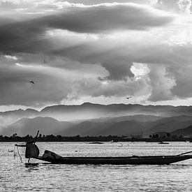 Zwart-wit foto van een visser die zijn netten ophaalt tijdens zonsondergang op het Inle meer in Myan van Twan Bankers