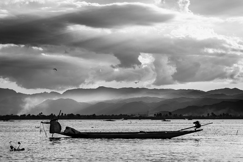 Zwart-wit foto van een visser die zijn netten ophaalt tijdens zonsondergang op het Inle meer in Myan van Twan Bankers