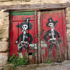 Rote Türen einer Scheune im spanischen Dorf Miranda del Castanar mit einer Zeichnung von zwei Skelet von Joost Adriaanse