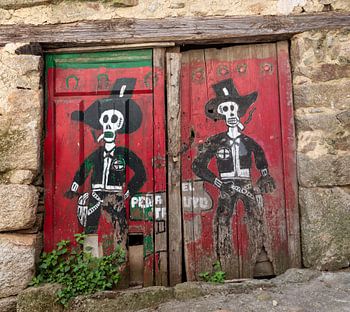 Red doors of barn in Spanish village of Miranda del Castanar with drawing of two skeleton cowboys