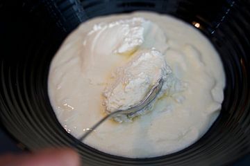 Spatel de room met een lepel door het kwark-yoghurtmengsel in een kom