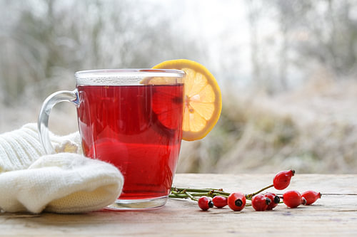 Heißer roter Hagebuttentee mit einer Zitronenscheibe in einem Glasbecher auf einem rustikalen Holzti