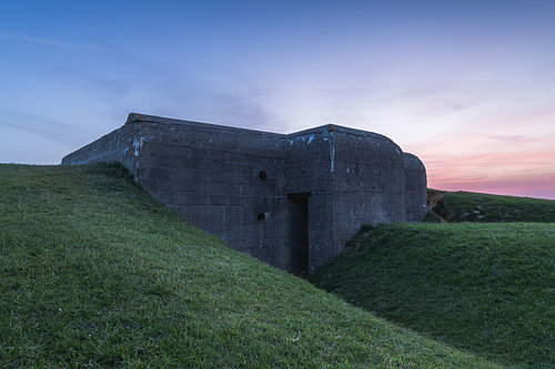 Historische Duitse bunker verscholen in het glooiende landschap van Longues-sur-Mer tijdens een rustige zonsopkomst aan de kust van Normandië in Frankrijk.