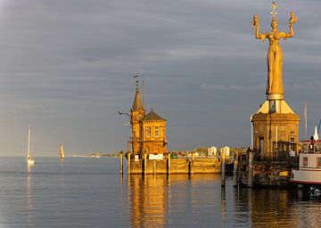 Konstanz aan het Bodenmeer, haveningang met Justizia, vuurtoren, schepen, weerspiegelingen bij oranje zonsondergang van Andreas Freund